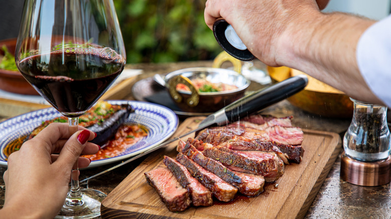 a woman holding a glass of red wine alongside steak
