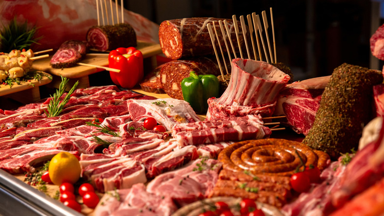 A variety of meats from steaks to sausages to pork chops and others,  are displayed artfully, interspersed with vegetables