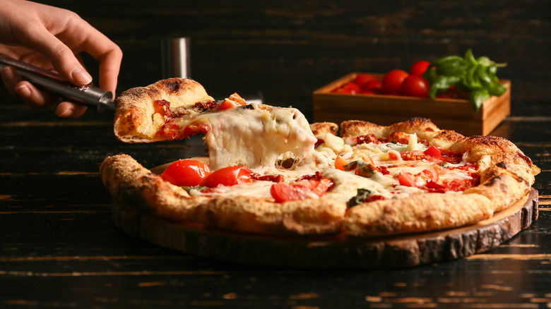 Hand lifting a slice from a cheesey whole pizza.