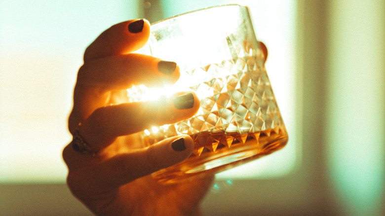 Hand holding glass of whisky backlit by sun