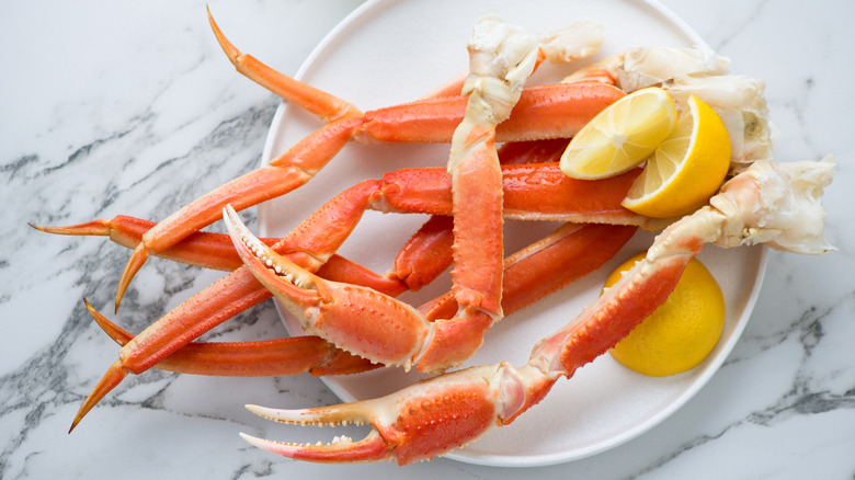Cooked crab legs and lemon wedges on a white plate on a marble countertop