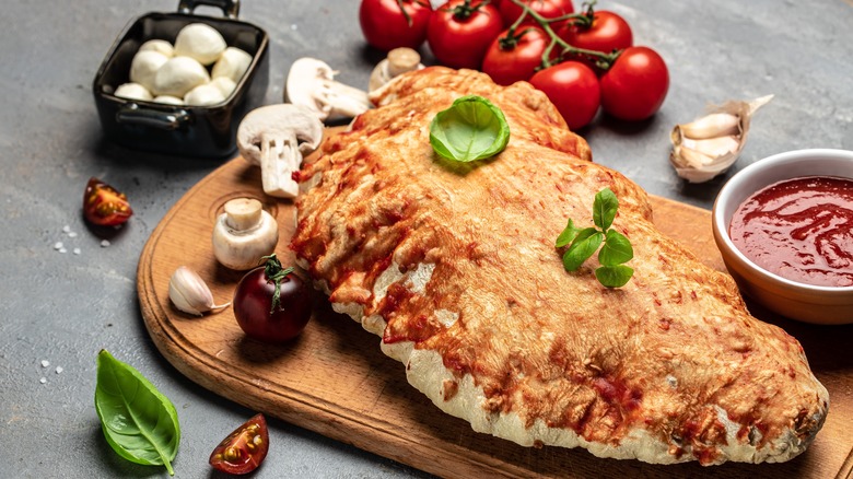 Calzone covered in cheese and surrounded by fresh veg and basil