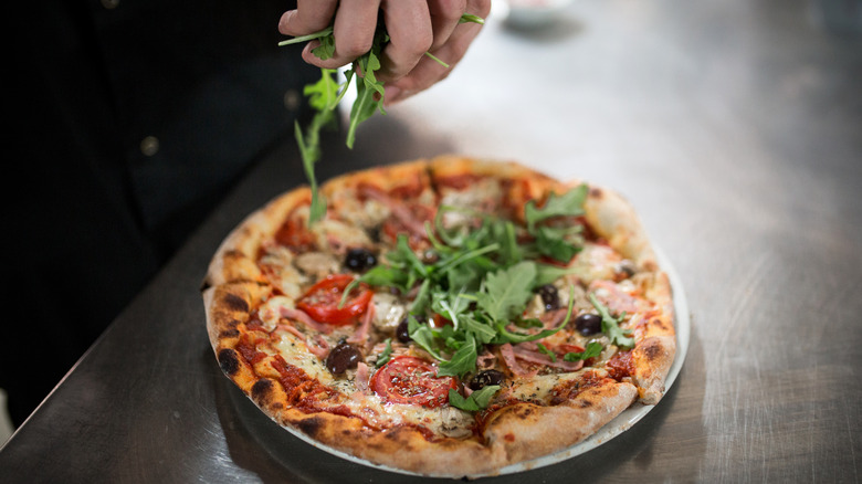 Person garnishing pizza with arugula