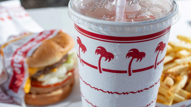 A close-up of a soft drink from In-N-Out with burgers and fries in the background.