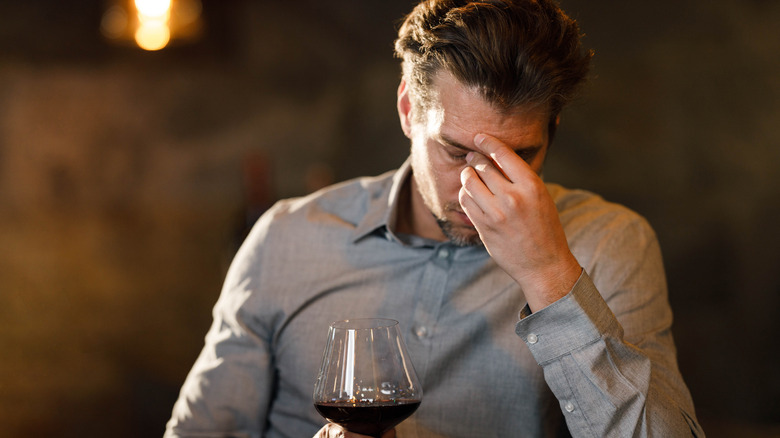 man with glass of wine holding head