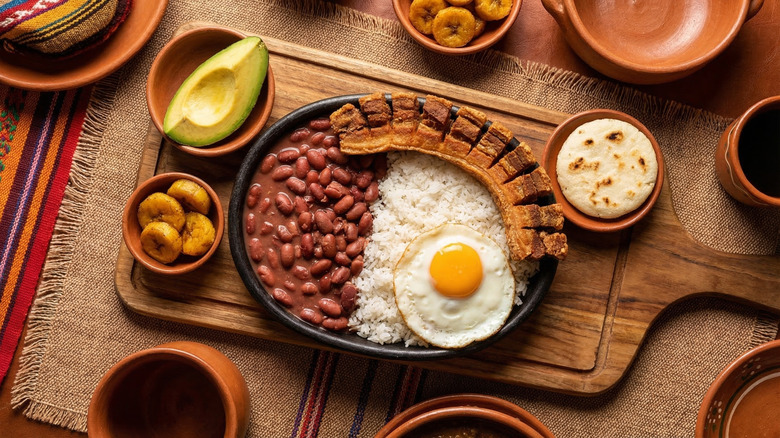Overhead view of board full of Bandeja Paisa with rice, a fried egg, beans, and pork