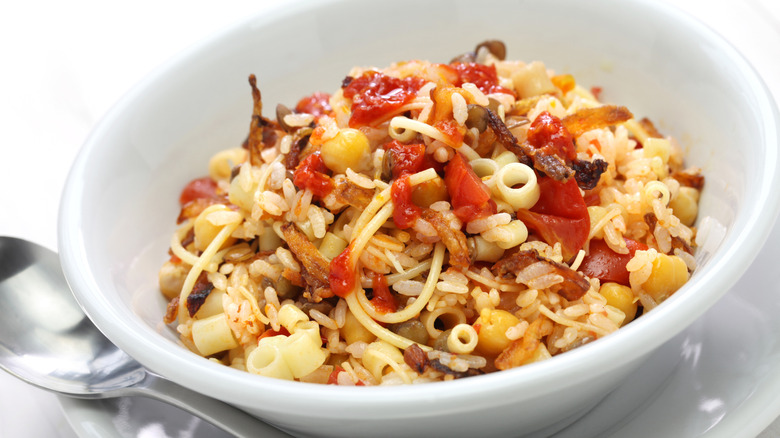 White bowl of Egyptian Koshari with rice, lentils, tomato sauce, and noodles