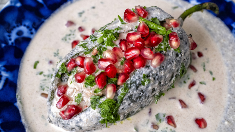 Plate of traditional Chiles en Nogada with a stuffed pepper, white cream sauce, and pomegranate seeds