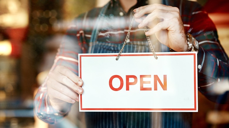 A shop owner puts an open sign with a white background and red lettering in a window