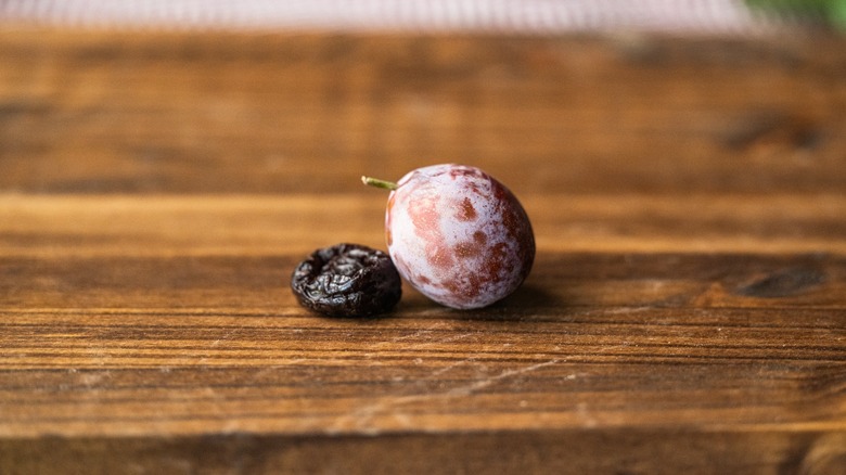 A fresh plum next to a dried prune on a wooden counter