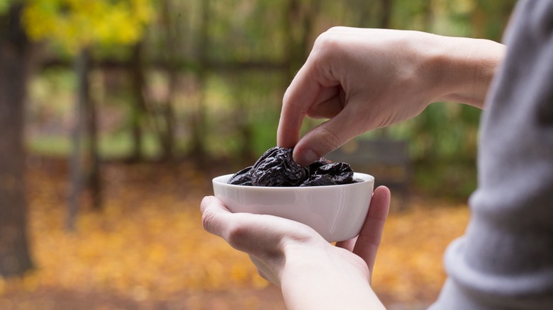 Man picking dried prunes from a bowl outside