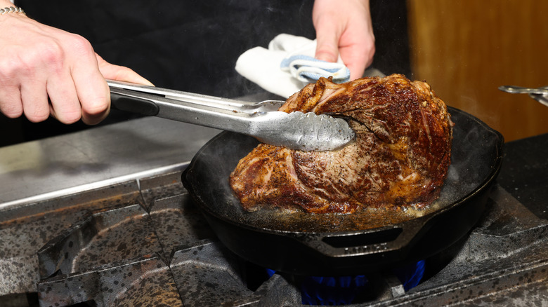 A cook flips a steak in a cast iron pan