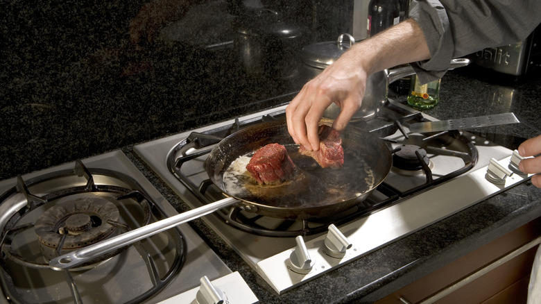 A cook tests a piece of meat in the pan with their hand
