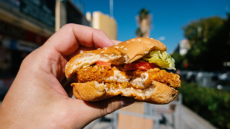 A person holds a fried chicken sandwich out on the street