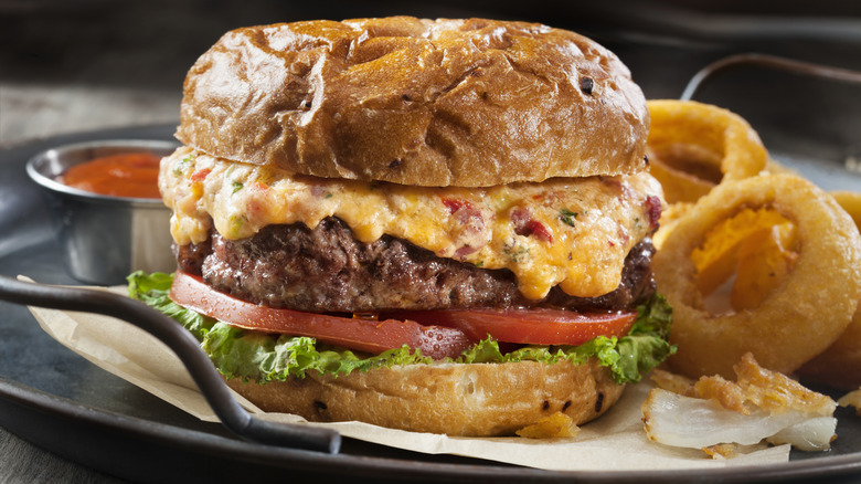 Cheeseburger topped with pimento cheese in a bun with onion rings