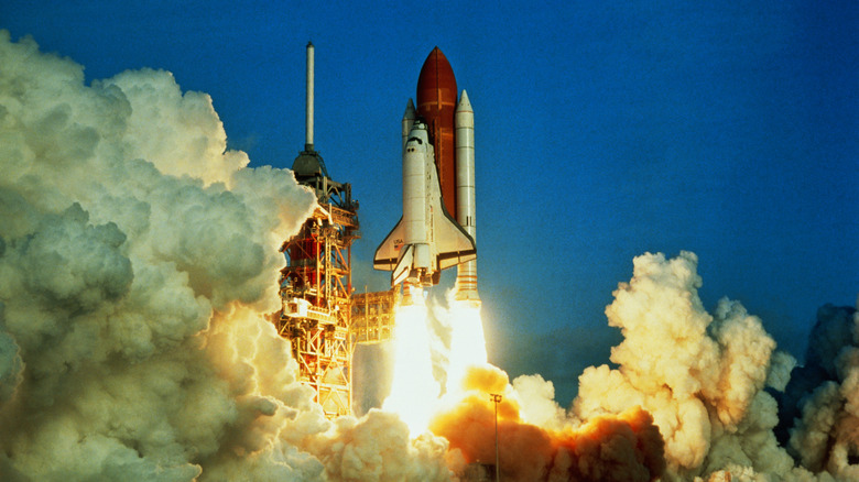 A NASA shuttle takes off, surrounded by plumes of smoke