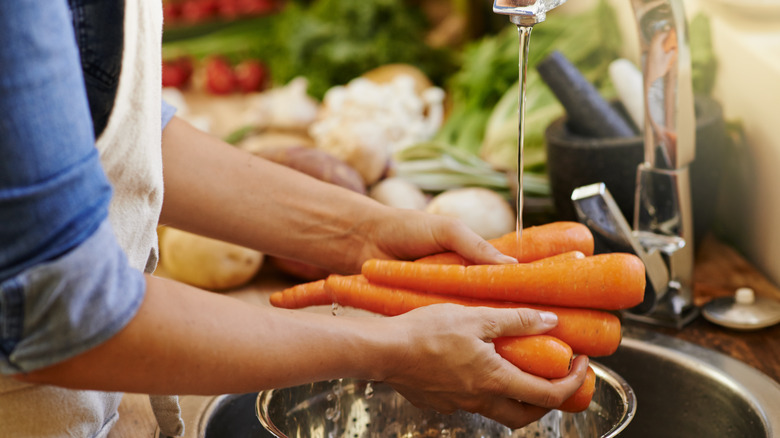 woman rinsing carrots in kitchen sink