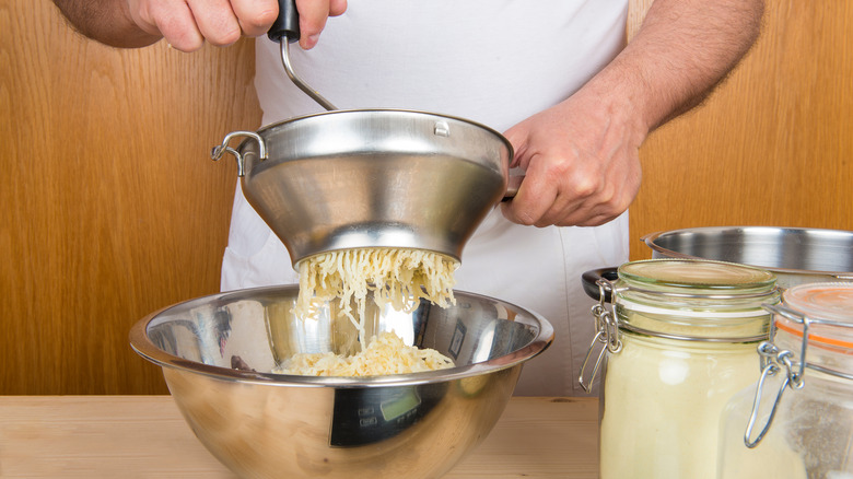 Hands cranking potatoes through a food mill into bowl