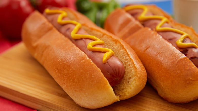 A close up of two hot dogs topped with mustard