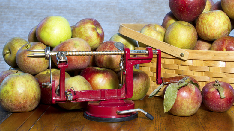 Apples next to an old-school, hand-crank peeler