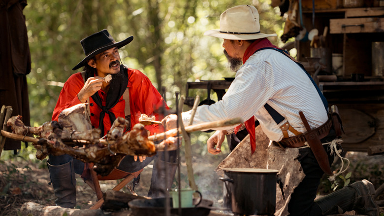 Cowboys sit around a campfire, enjoying a meal