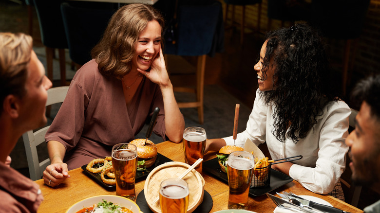 Friends dining around a table, laughing and talking around food, with elbows on the table