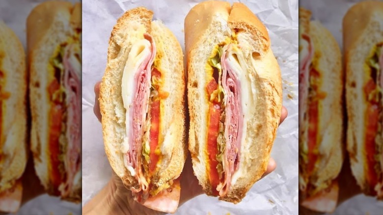 Hands holding two cut halves of an Italian combo sandwich