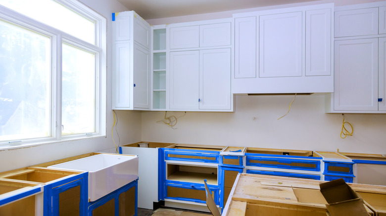 kitchen remodeling in progress, with paint tape on the cupboards