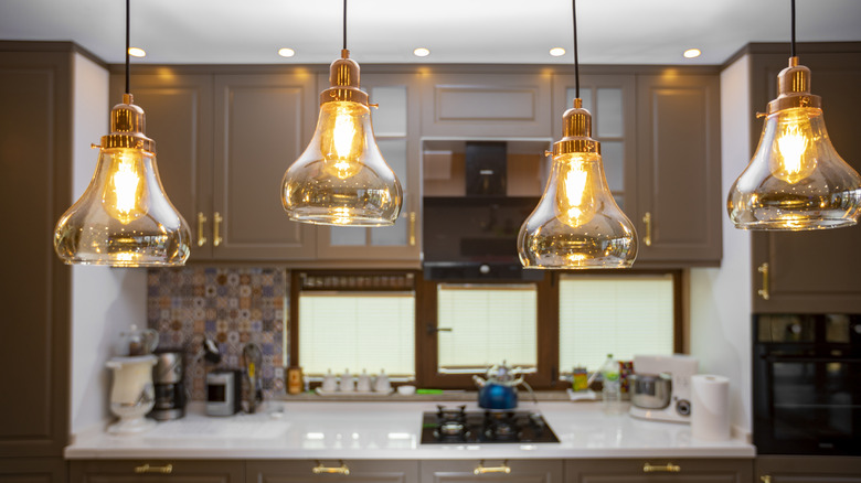 A retro looking kitchen has open glass pendant lights hanging from the ceiling in the foreground