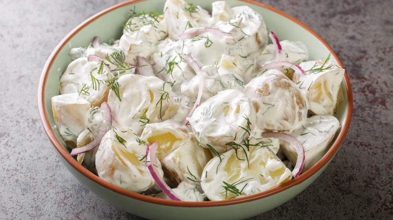 Creamy potato salad sits in a green bowl with a red rim