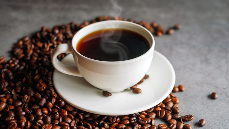Steaming cup of coffee surrounded by coffee beans