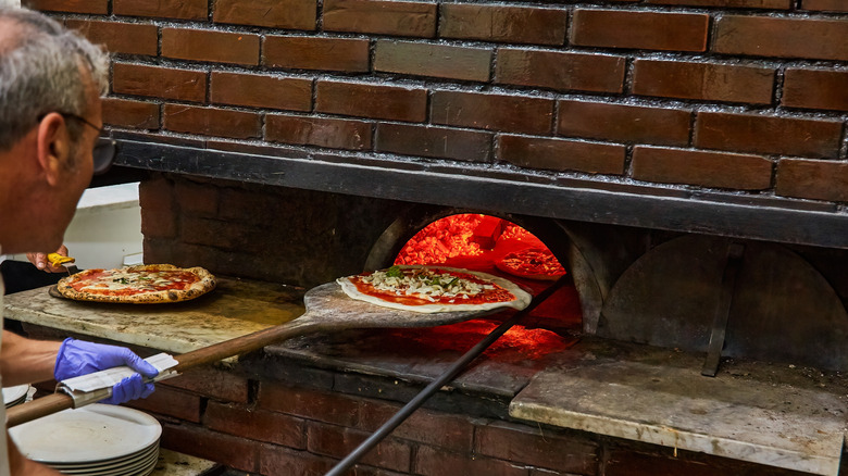A pizza-maker slides a pizza into a brick oven