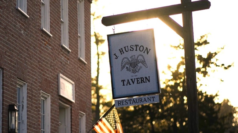 Sign for J. Huston Tavern hanging from a post framed by the sun