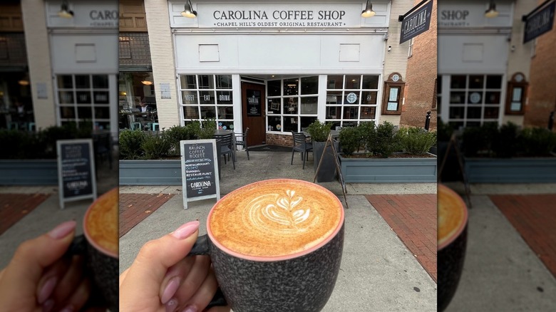 Hand holding a mug with decorative latte art outside Carolina Coffee Shop