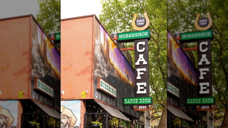 Large sign juts out from the mural-painted wall of the Horseshoe Cafe