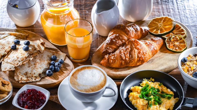 A well-spread breakfast table with juice, coffee, crepes, croissants, eggs, and more