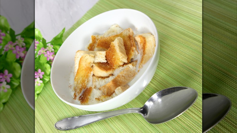 A white bowl containing milk toast sits on a green placemat next to flowers and a silver spoon