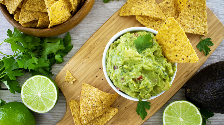 Fresh guacamole with tortilla chips, fresh lime, and cilantro.