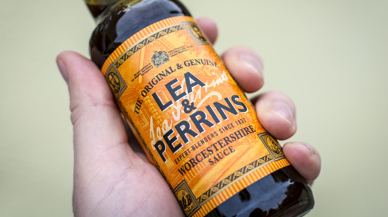 A hand holding Lea & Perrins Worcestershire sauce.