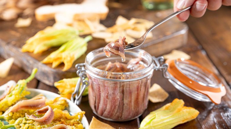 Anchovies in a jar, on a wooden rustic background with squash blossoms.