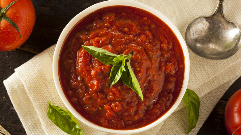 Marinara in a white bowl topped with basil next to a silver spoon