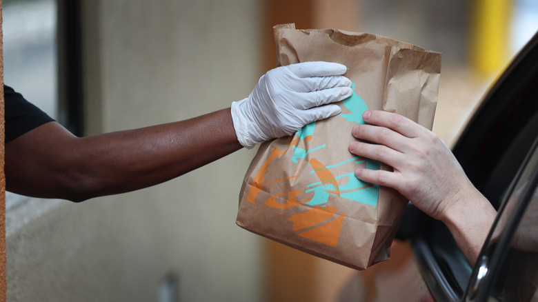 A Taco Bell worker hands a drive-thru customer food.