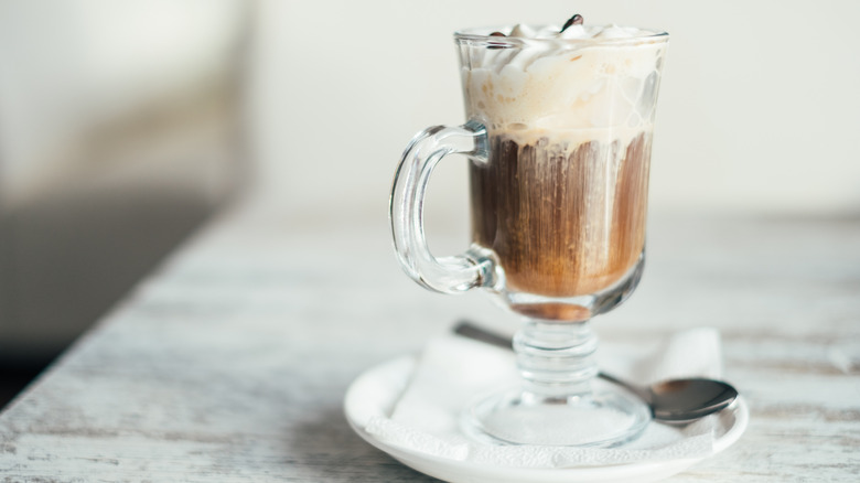 An Irish coffee with whipped cream in a glass mug.