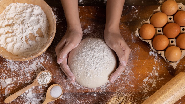 Person kneading dough next to eggs and a bowl of flour