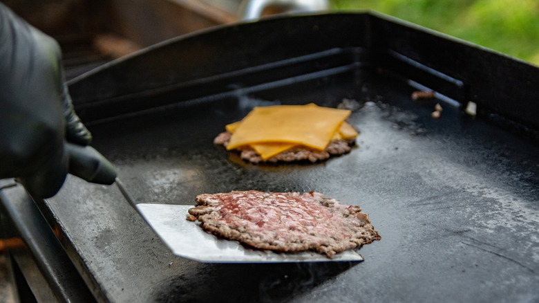Cook making smash burgers on a griddle