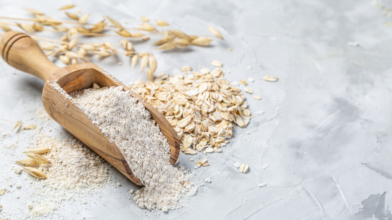 Wooden scoop of oat flour next to oats