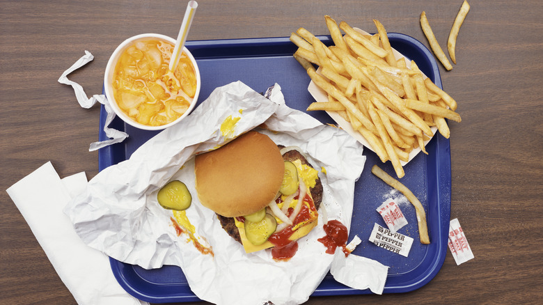 Burger, fries, and a drink on a blue plastic tray with salt, pepper, and napkins on it