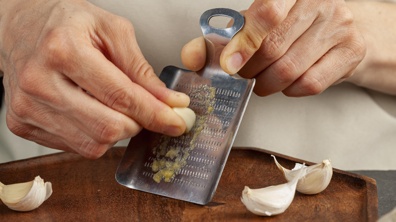 Two hands grates a garlic glove on a small metal grate microplane zester