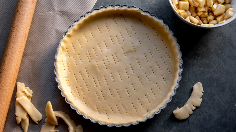 Pie dough in tin next to rolling pin