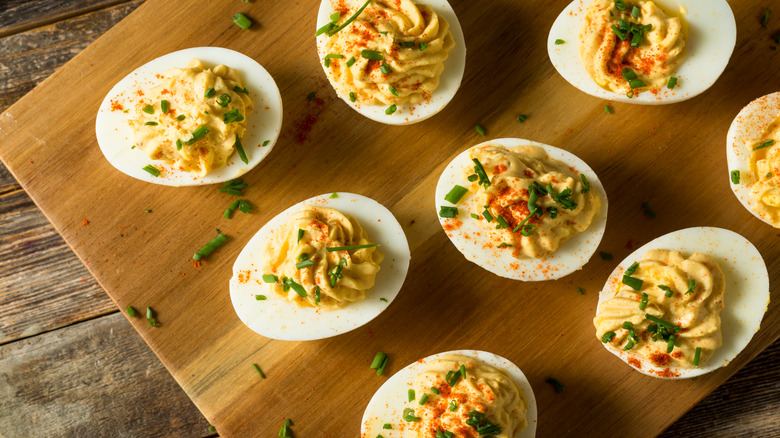 Deviled eggs on a wooden board with paprika and chive garnish 